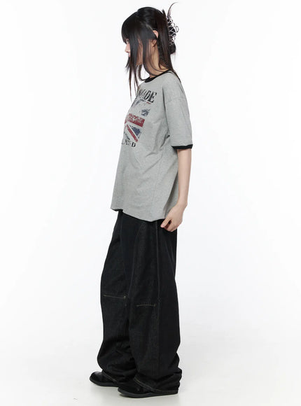 Graphic Short Sleeve Tee CU519 in gray, side view on model, showing relaxed boxy silhouette and black ringer trim at collar and sleeves, paired with dark wide-leg jeans.