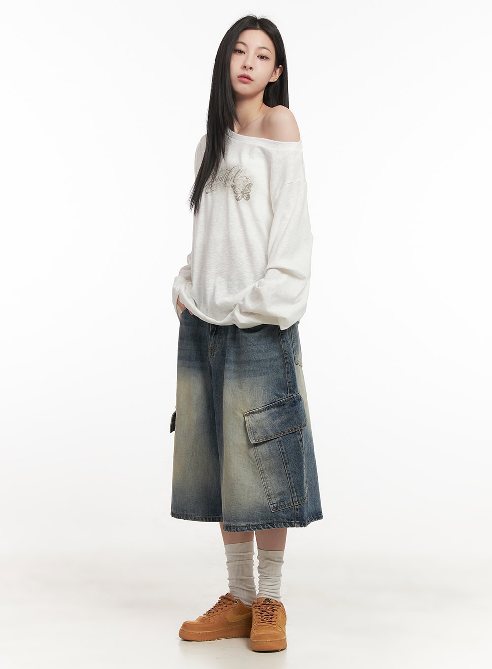 Cargo Bermuda Denim Shorts CF514 in dark blue, three-quarter side view on model, wide-fit washed denim with flap cargo pocket visible, styled with white off-shoulder top and tan sneakers.