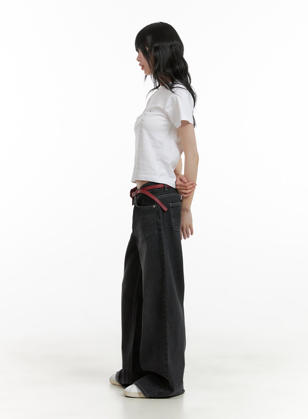 Low Rise Baggy Jeans CU410 in black, full-body side profile on model, floor-grazing wide leg washed denim, low rise waistband, styled with white crop tee and red belt.