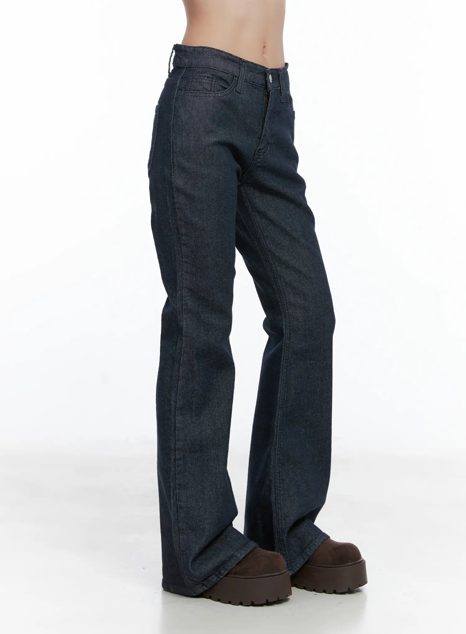 Kinley Flare Jeans CS502 in dark indigo, side view on model, full-length silhouette showing gradual flare from knee, long inseam, paired with chunky brown boots.