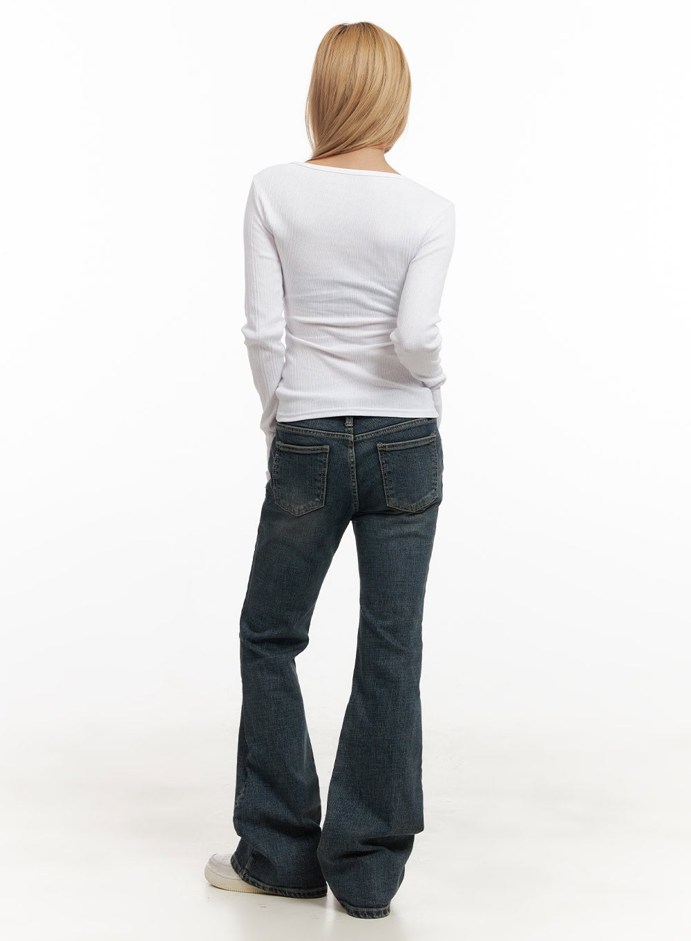 Natalia Low-Rise Flared Jeans CJ508 in dark blue, full back view on model, low-rise washed denim with back patch pockets and flared hem pooling at sneakers, worn with white ribbed long-sleeve top.