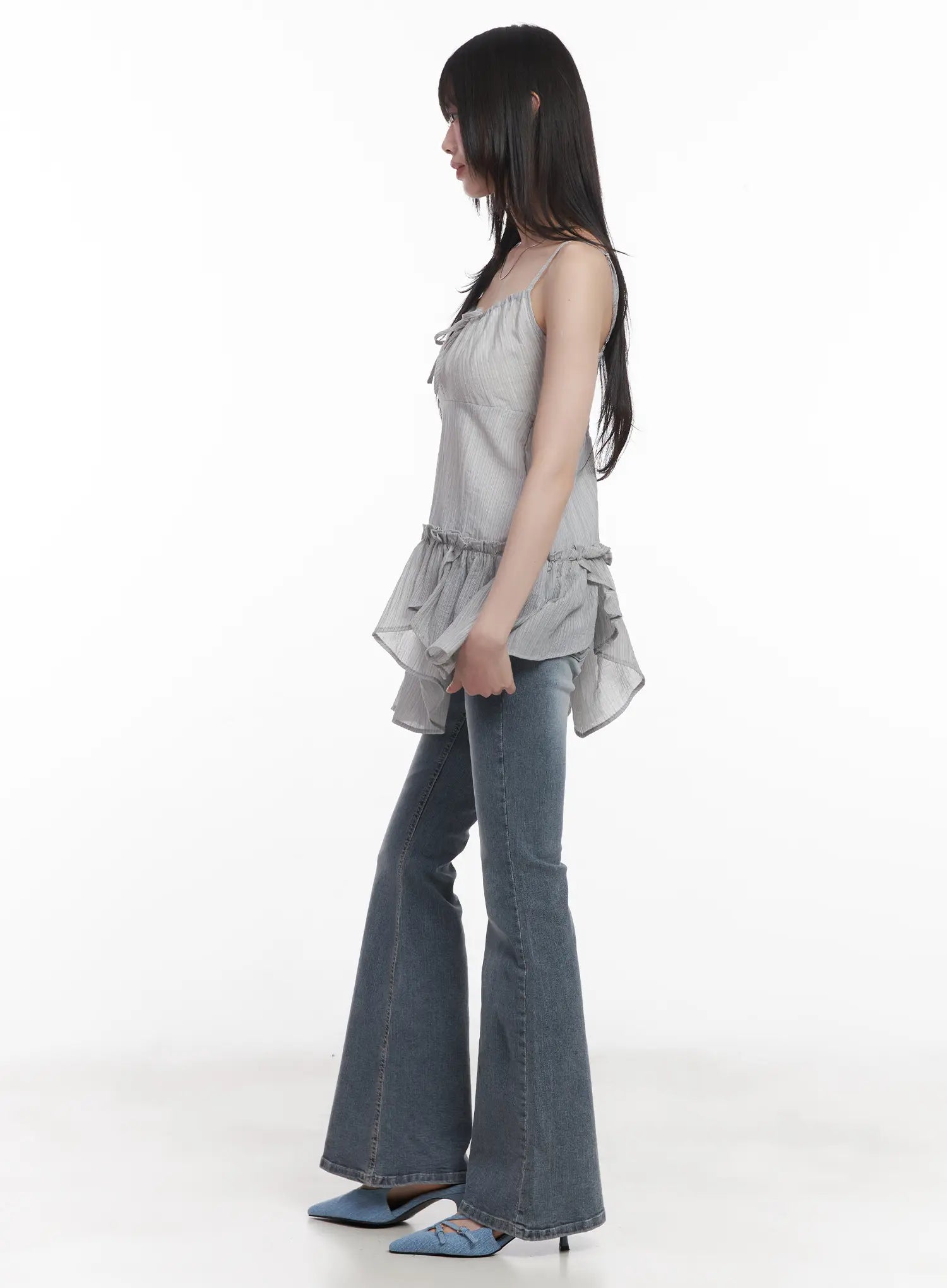 Soyeon Flared Jeans with Hip Pads CU520 in dark gray, side view on model, washed bootcut silhouette highlighting slim thigh and flared leg, styled with ruffle cami and blue mules.