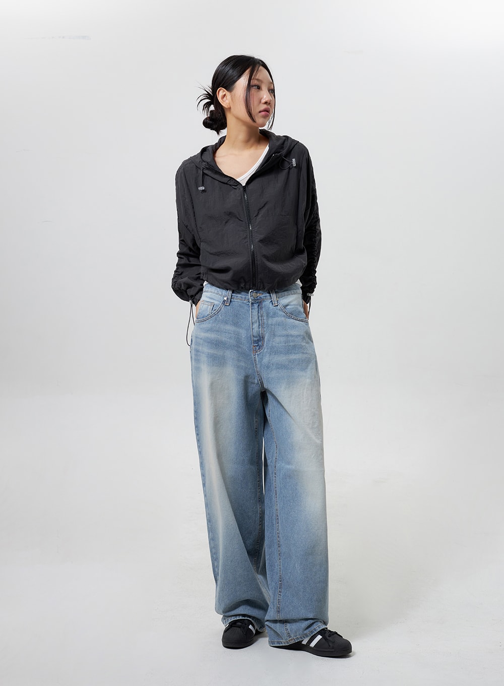 Low Rise Baggy Jeans CY324 in light blue, full-length three-quarter front view on model looking aside, relaxed baggy wide-leg denim, paired with black hooded windbreaker and sneakers.