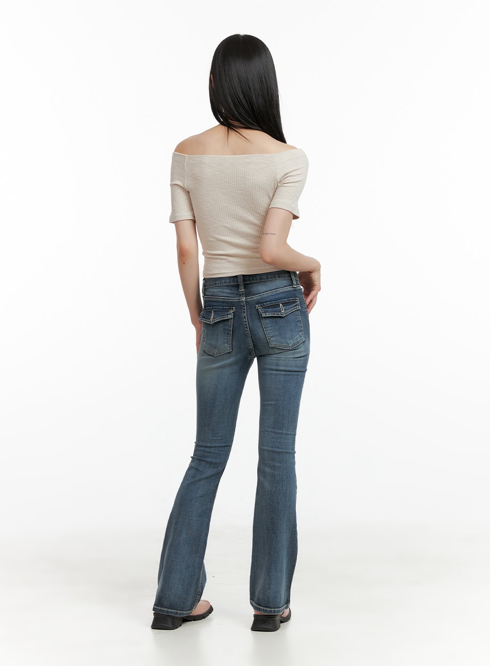 Tight Fit Low Waist Bootcut Jeans CL403 in dark blue, back full-length view on model, flap back pockets with contrast stitching, bootcut flare, styled with beige off-shoulder crop top.