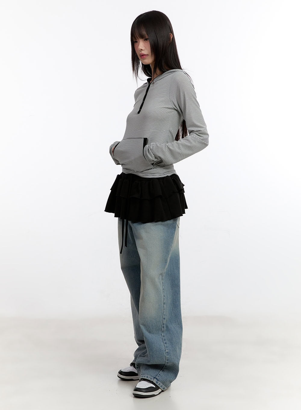 Jillie Washed Baggy Jeans CA508 in blue, 3/4 side view on model looking down, oversized washed denim leg silhouette visible, styled with striped hooded top and layered ruffle skirt.