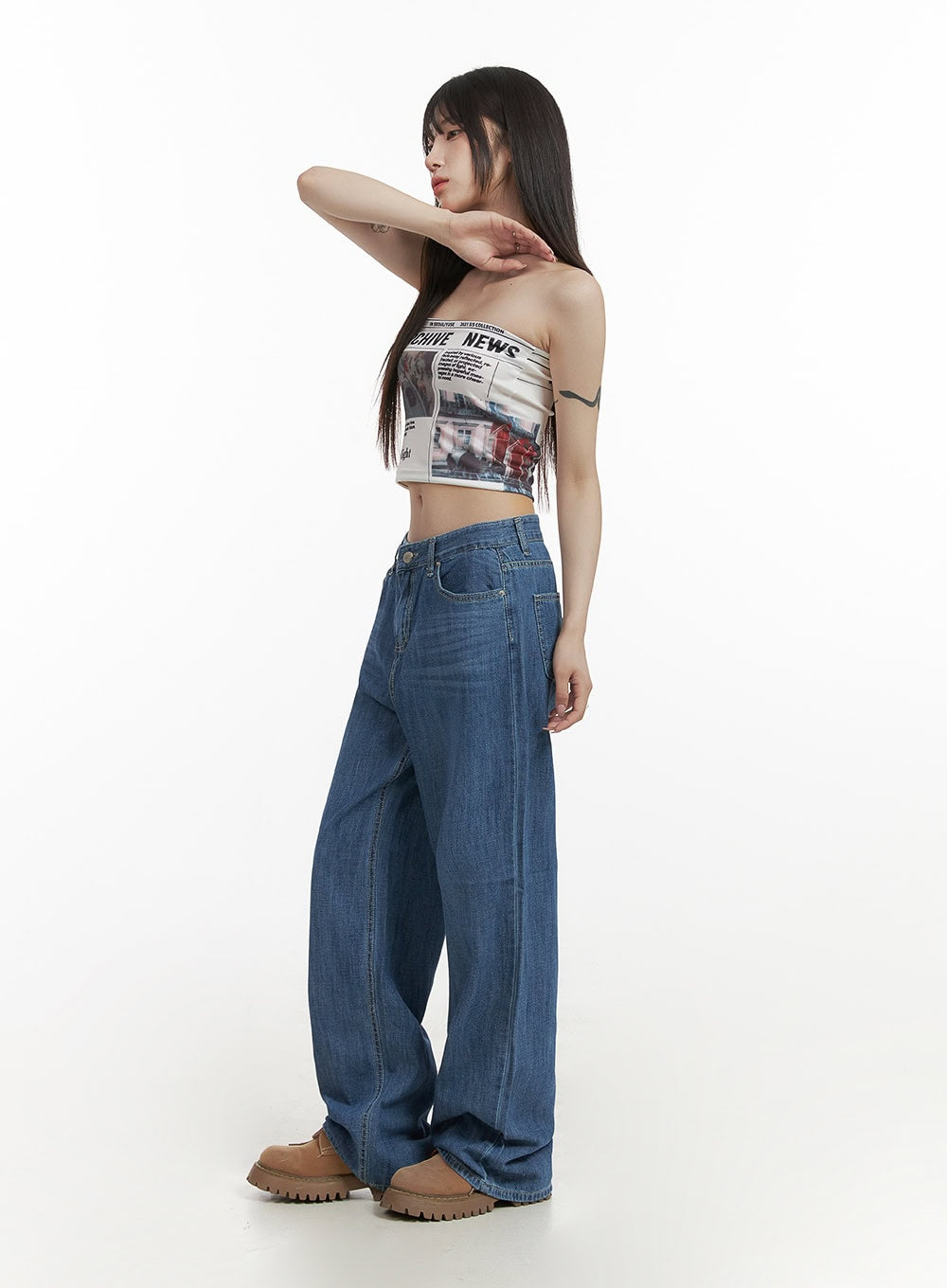 Solid Low Rise Baggy Jeans CY407 in blue, side profile on model with arm raised, low-rise wide-leg washed denim, paired with graphic bandeau crop top and tan chunky boots.