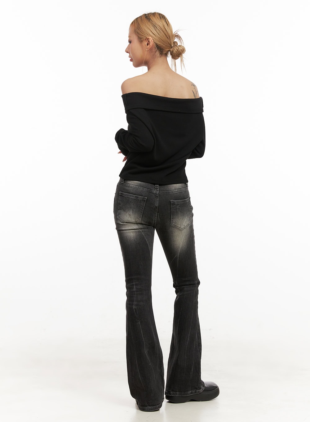 Georgina Low-Rise Flared Jeans CJ507 in black, full-body back view on model, back patch pockets with faded wash detail, flared hem pooling at floor, styled with black off-shoulder knit and platform shoes.