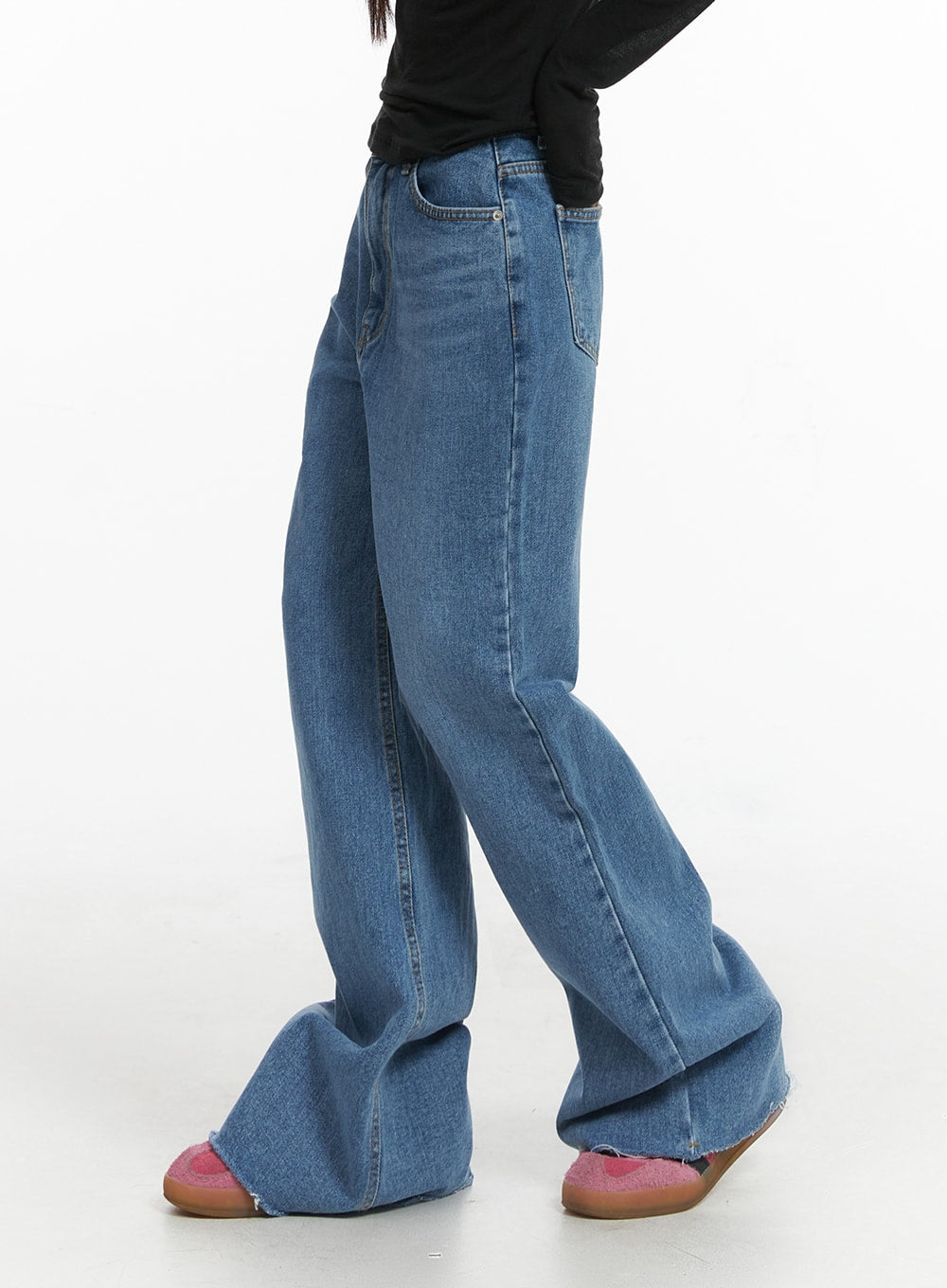 Blue Denim Bootcut Jeans CJ431 in blue, side close-up on model, highlighting wide flare from knee, raw-cut frayed hem and washed denim texture, paired with black long sleeve top and pink mules.