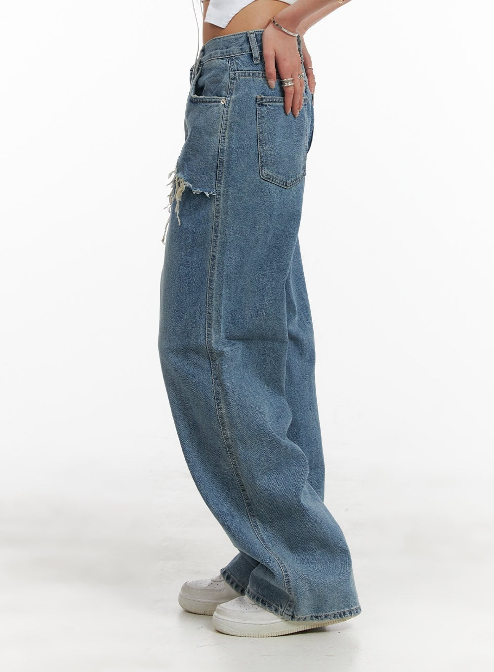 Layered Wide Leg Jeans CA430 in Blue, side view on model, showing destroyed frayed layered hem silhouette at hip, wide-leg washed denim fall to floor, back pocket visible.