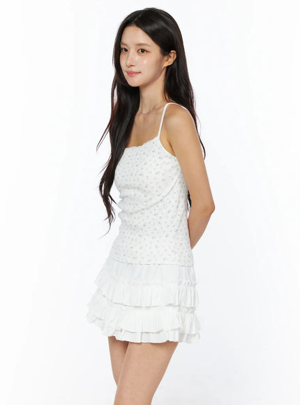 Floral Ribbed Cami Top CU522 in white, side view on model, thin spaghetti straps and fitted ribbed silhouette with all-over floral print, styled with white ruffle mini skirt.