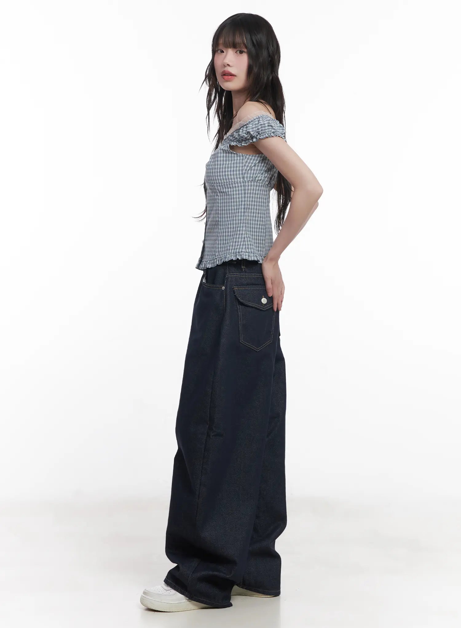 Hyein No-Fade Relaxed-Fit Jeans CU519 in dark blue, side full-length view on model, wide-fit cotton denim with side flap pocket, styled with gingham off-shoulder top and white sneakers.