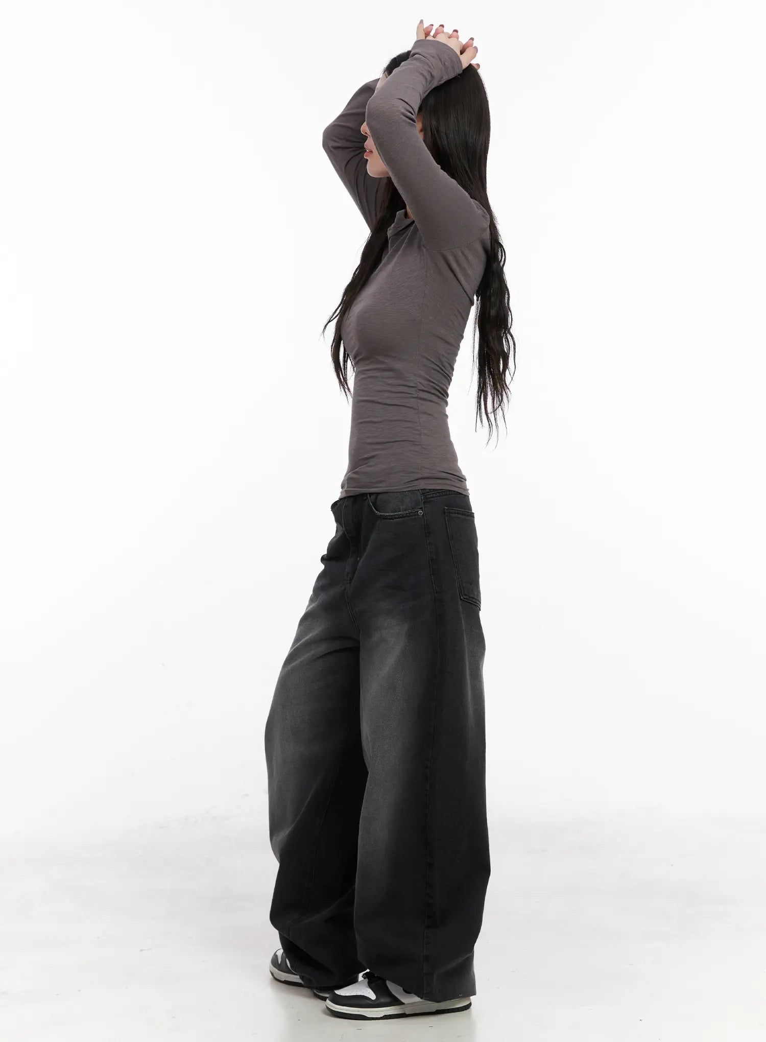 Yuji Dark-Washed Baggy Jeans CN513 in black, side profile on model with arms raised, acubi-style ultra-wide cotton denim, low-rise waistband and dramatic balloon leg, styled with gray top and sneakers.