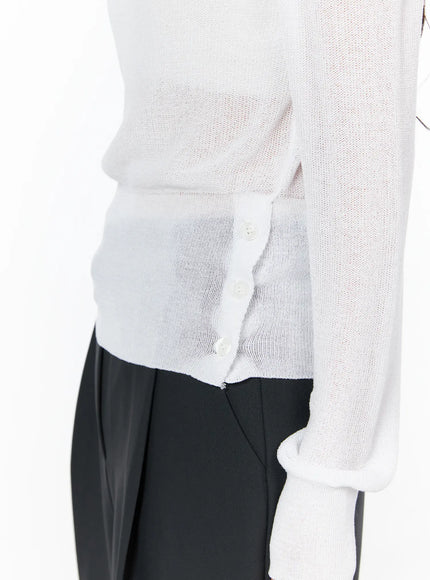 One-Shoulder Knit Top CU522 in white, side detail close-up on model, showing three-button side hem closure and sheer fine-knit fabric, paired with black trousers.