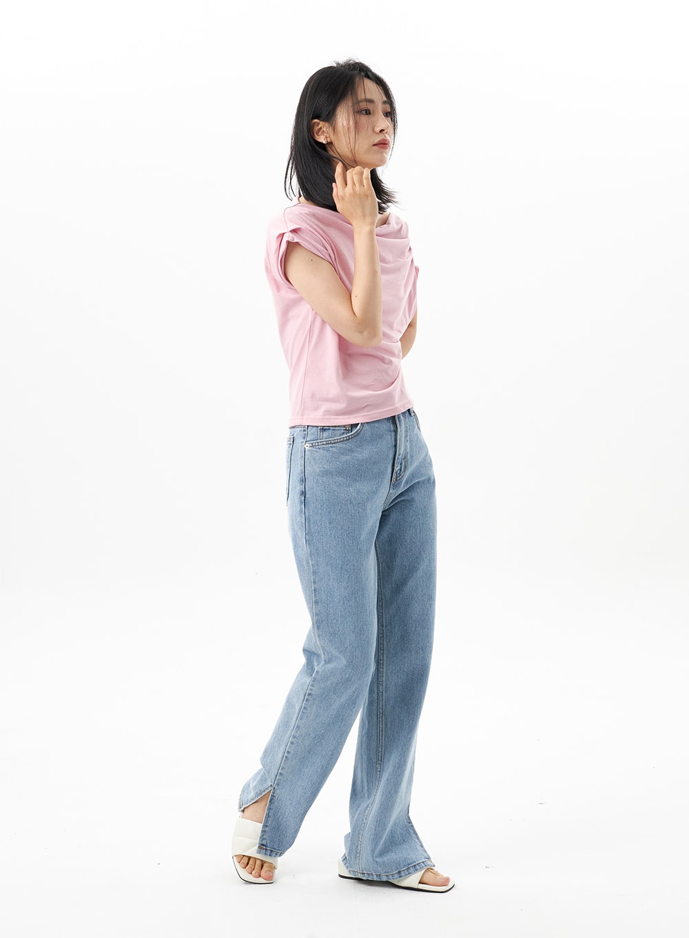 Slit Detail Jeans OU314 in blue, three-quarter side shot on model with slight walking pose, hem slit visible at ankle, paired with pink draped top and white sandals.