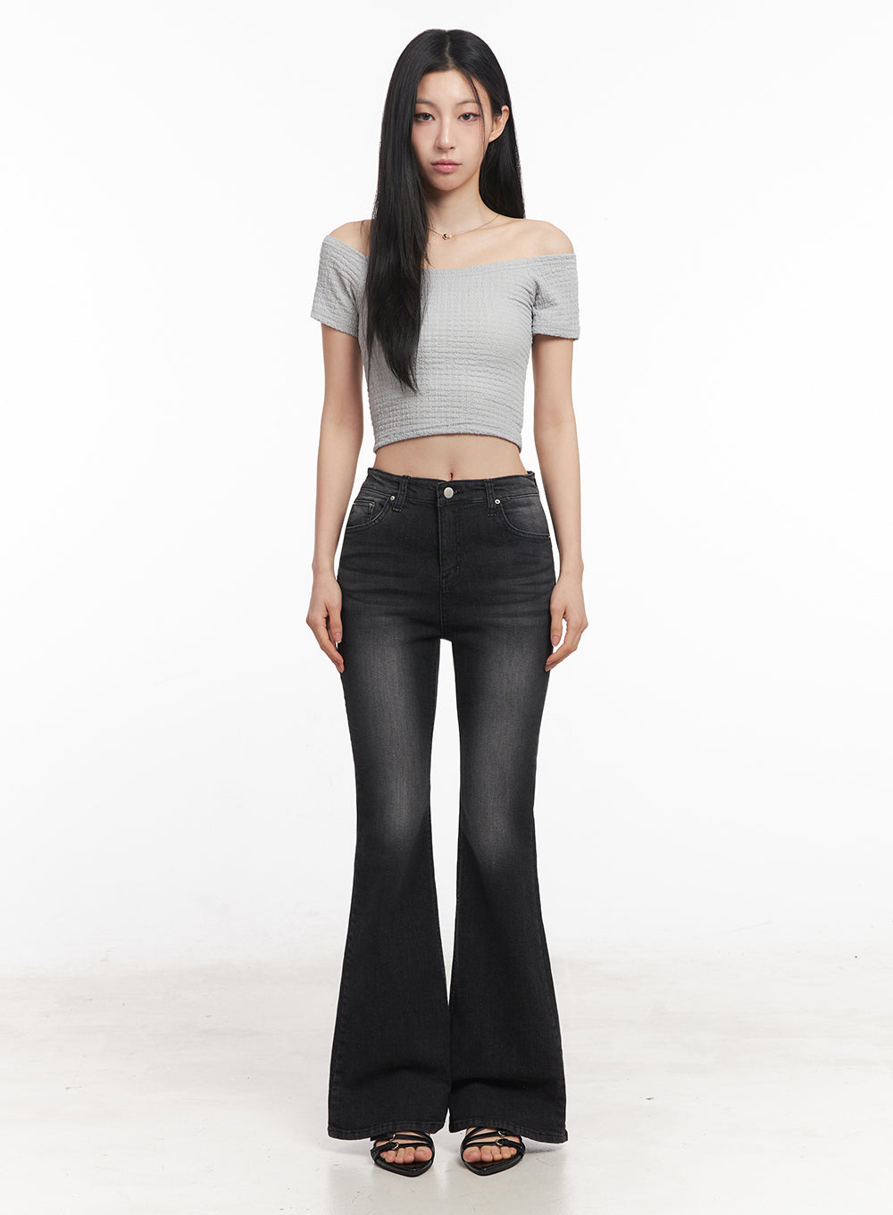 Lior Slim-Fit Bootcut Jeans IY516 in black, full-length front shot on model standing straight, high-rise washed bootcut denim, paired with grey off-shoulder crop top and black heeled sandals.