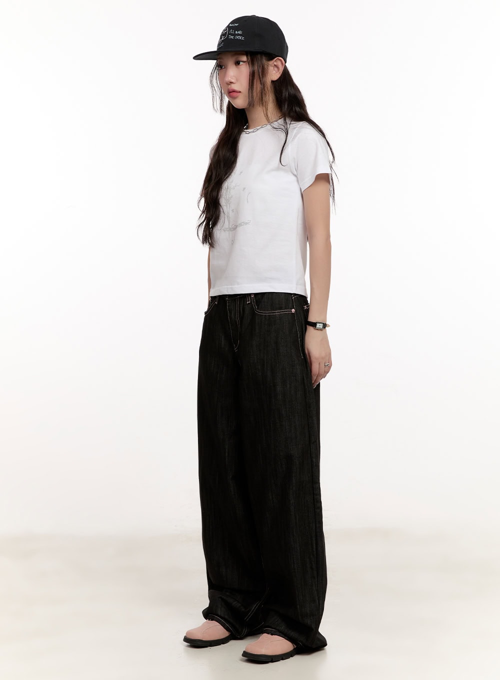 Trinity Stitched Baggy Jeans CM510 in black, three-quarter side view on model, floor-grazing wide leg denim, paired with white crop tee, black cap, and pink mule shoes.