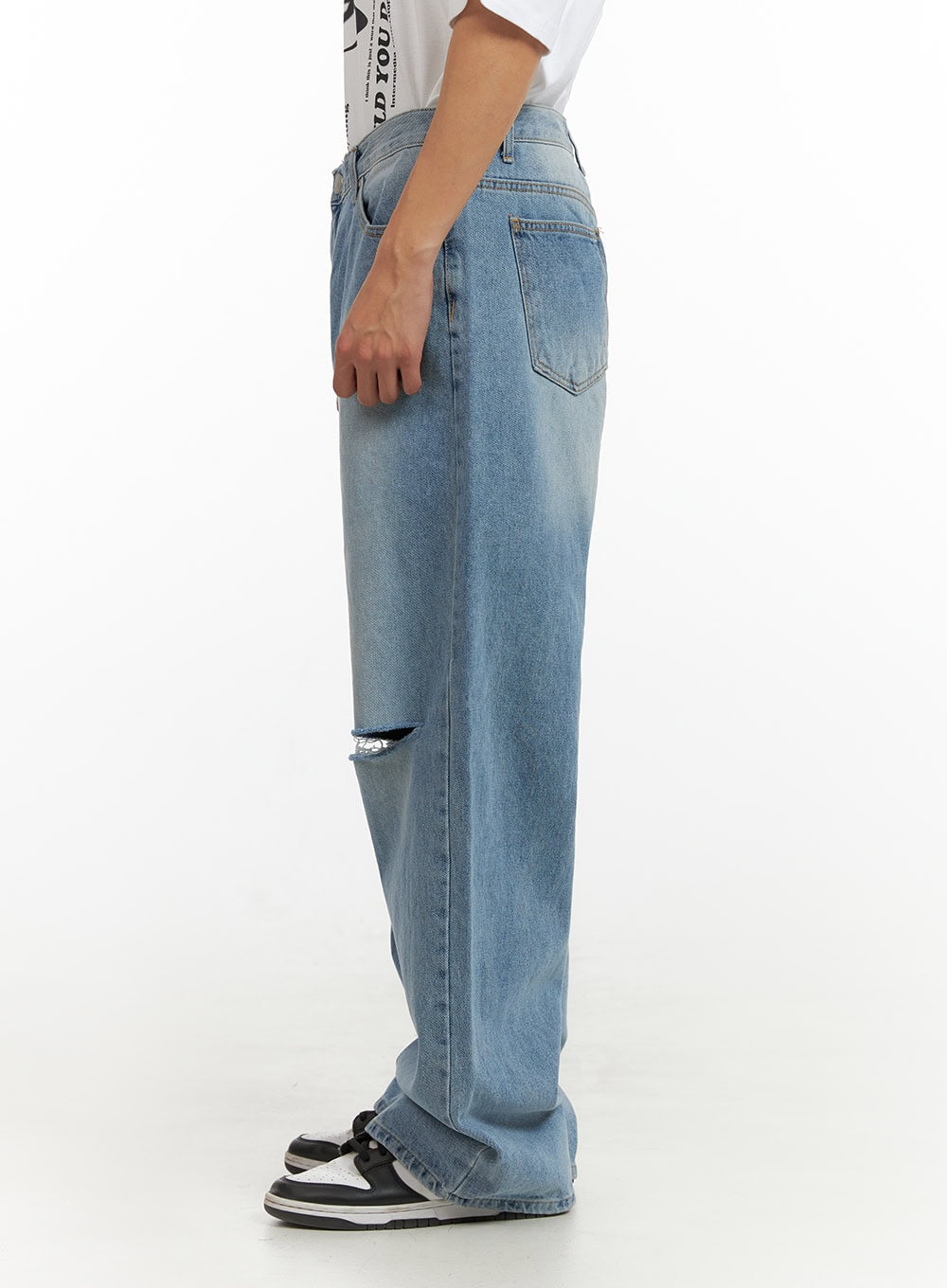 Men's Cut Out Baggy Jeans IU419 in blue, side view on model showing wide-leg silhouette, knee cut-out, back pocket, and relaxed fit, paired with white tee and sneakers.