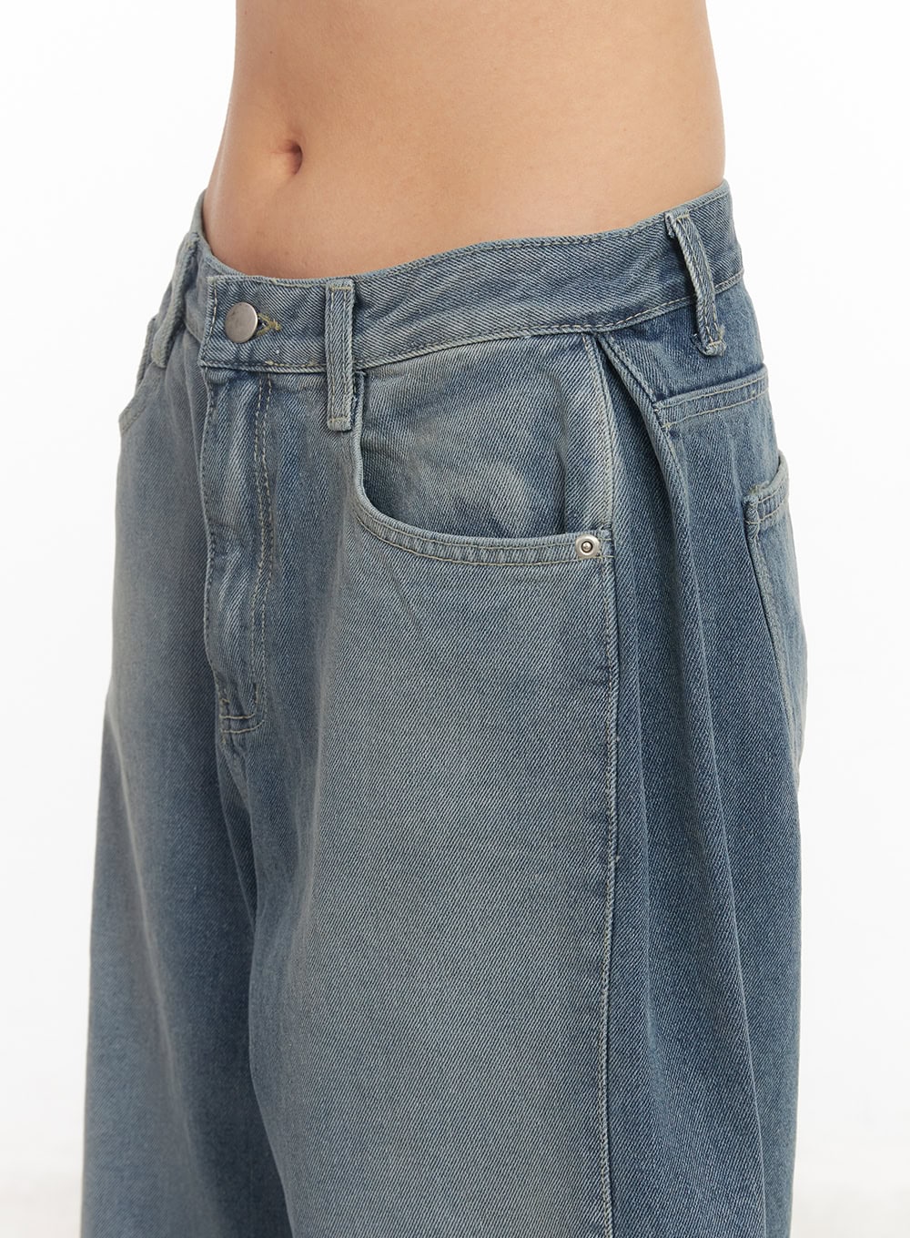 Amber Pintuck Wide-Leg Jeans CM511 in blue, close-up detail of waistband and front pocket on model, pintuck pleat, button closure, washed cotton denim texture.