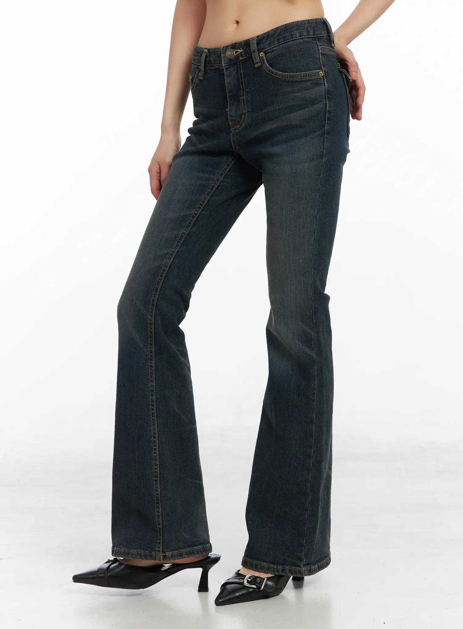 Kai Vintage Washed Flare Jeans CD515 in dark indigo, side view on model, low-rise bootcut silhouette with flared hem, gold contrast stitching, paired with black kitten-heel mules.