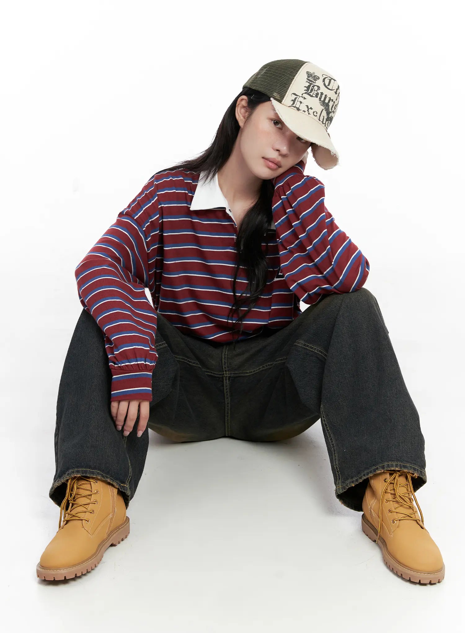 Leona Vintage Baggy Jeans CS526 in dark blue, seated editorial pose on model, baggy wide-leg cotton denim with amber washed fade, styled with striped polo and cap.