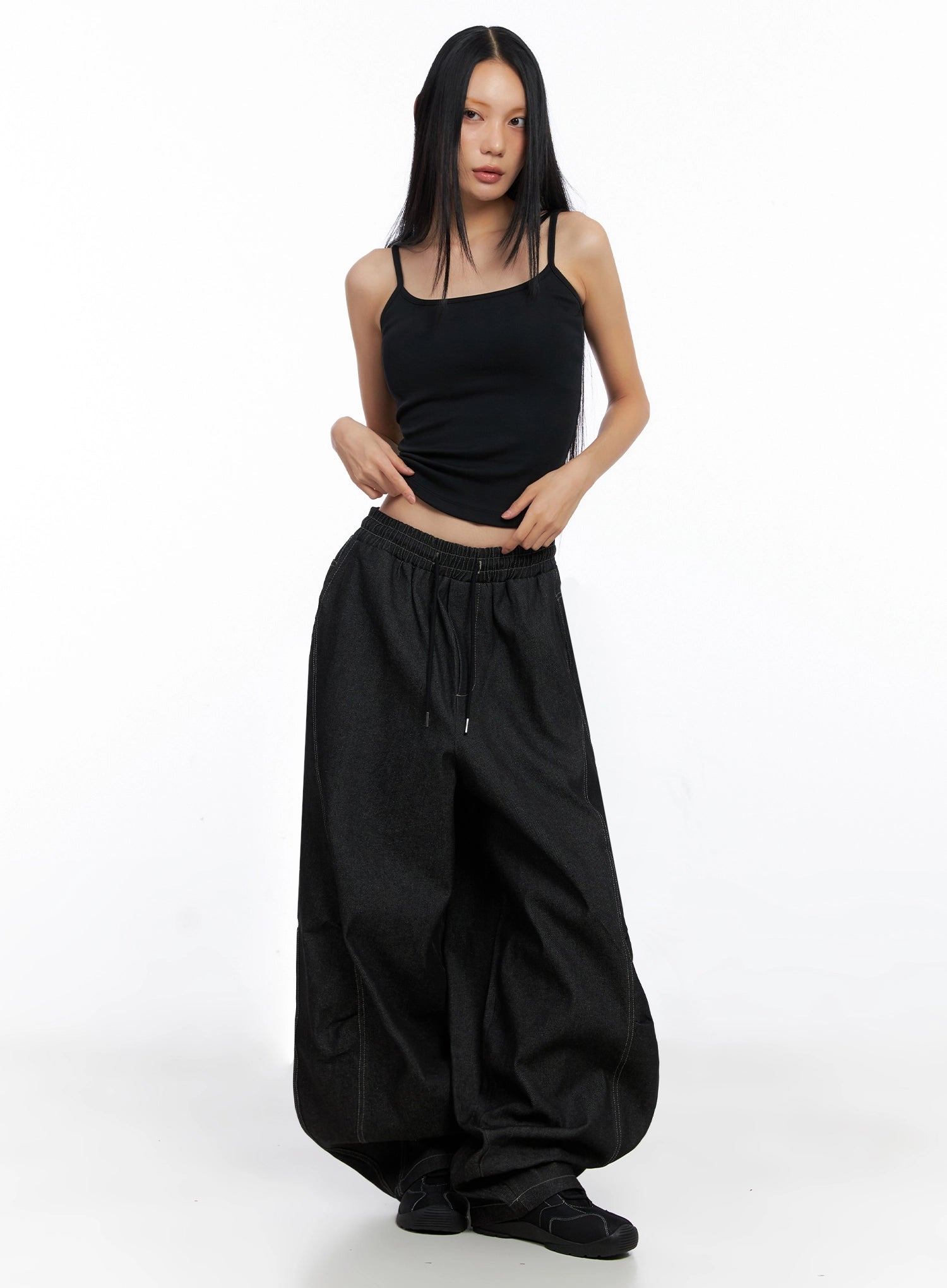 Ayra Graphic Baggy Jeans IO516 in Black, front three-quarter on model, oversized wide-fit cotton denim, low-rise elastic drawstring waist, voluminous leg pooling at sneakers, styled with black cami.