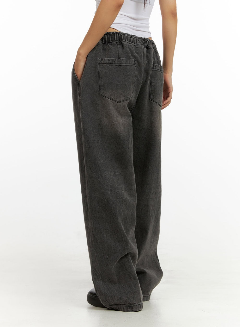 Banding Baggy Jeans IU412 in washed black, rear three-quarter view on model, back patch pockets and elastic waistband shown, wide baggy washed denim leg, styled with white top.