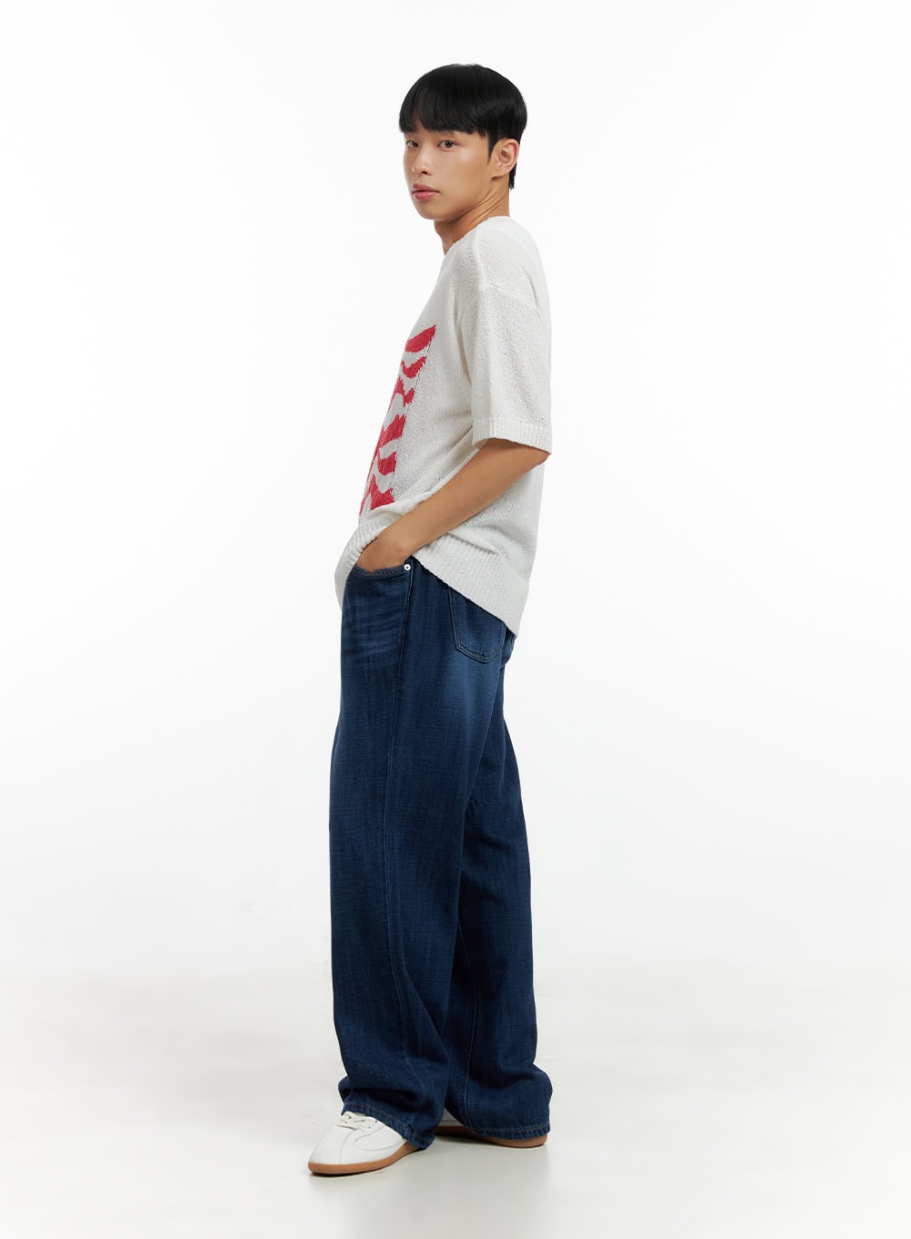 Men's Washed Cotton Denim Jeans CL429 in dark blue, three-quarter side view on male model, relaxed wide-leg cut, washed denim, styled with white graphic knit tee and white sneakers.