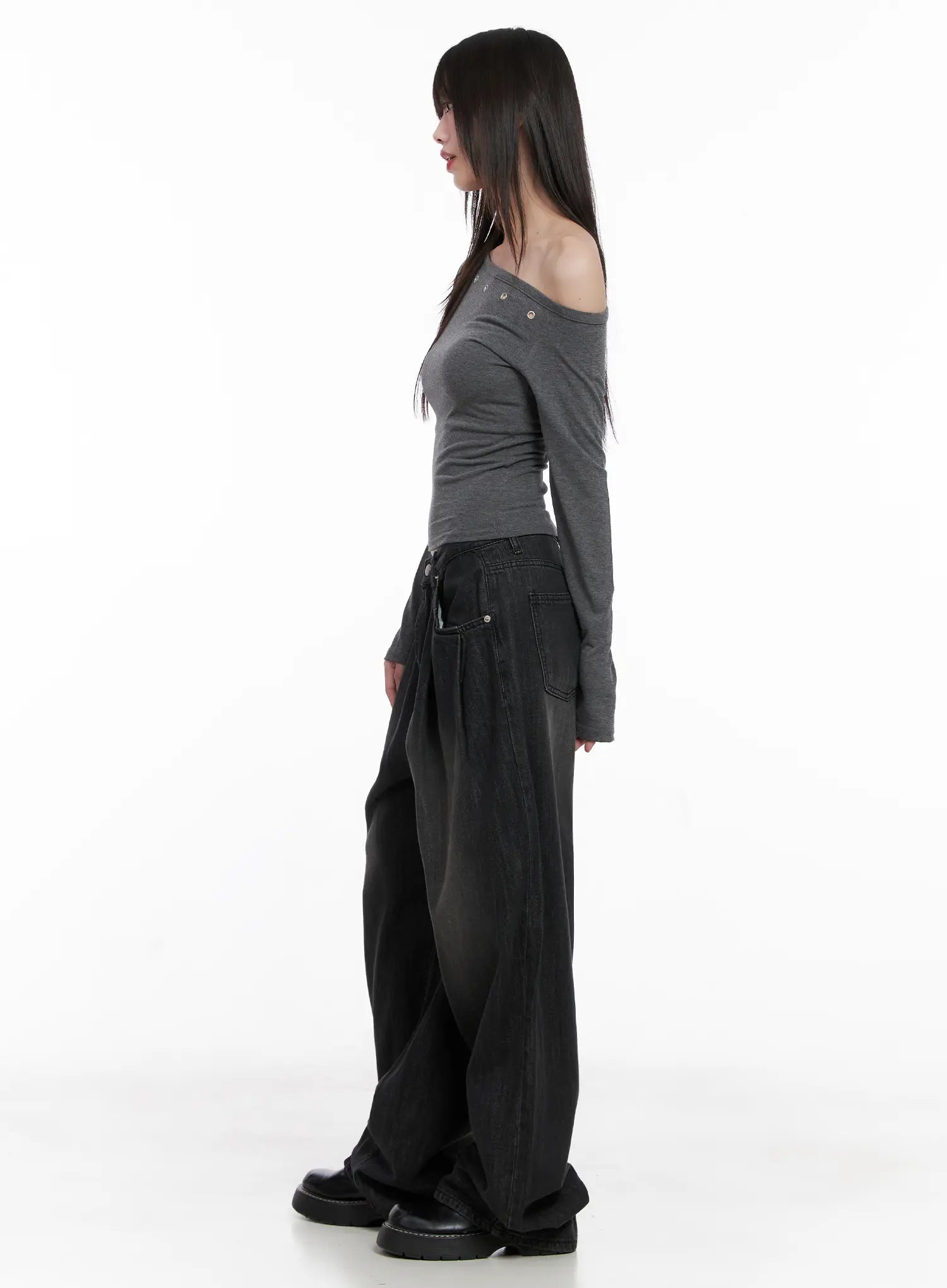 Elen Pintuck Baggy Jeans CG519 in black, side full-length view on model, pintuck pleat and low-rise waist visible, styled with gray off-shoulder long-sleeve top and black boots.