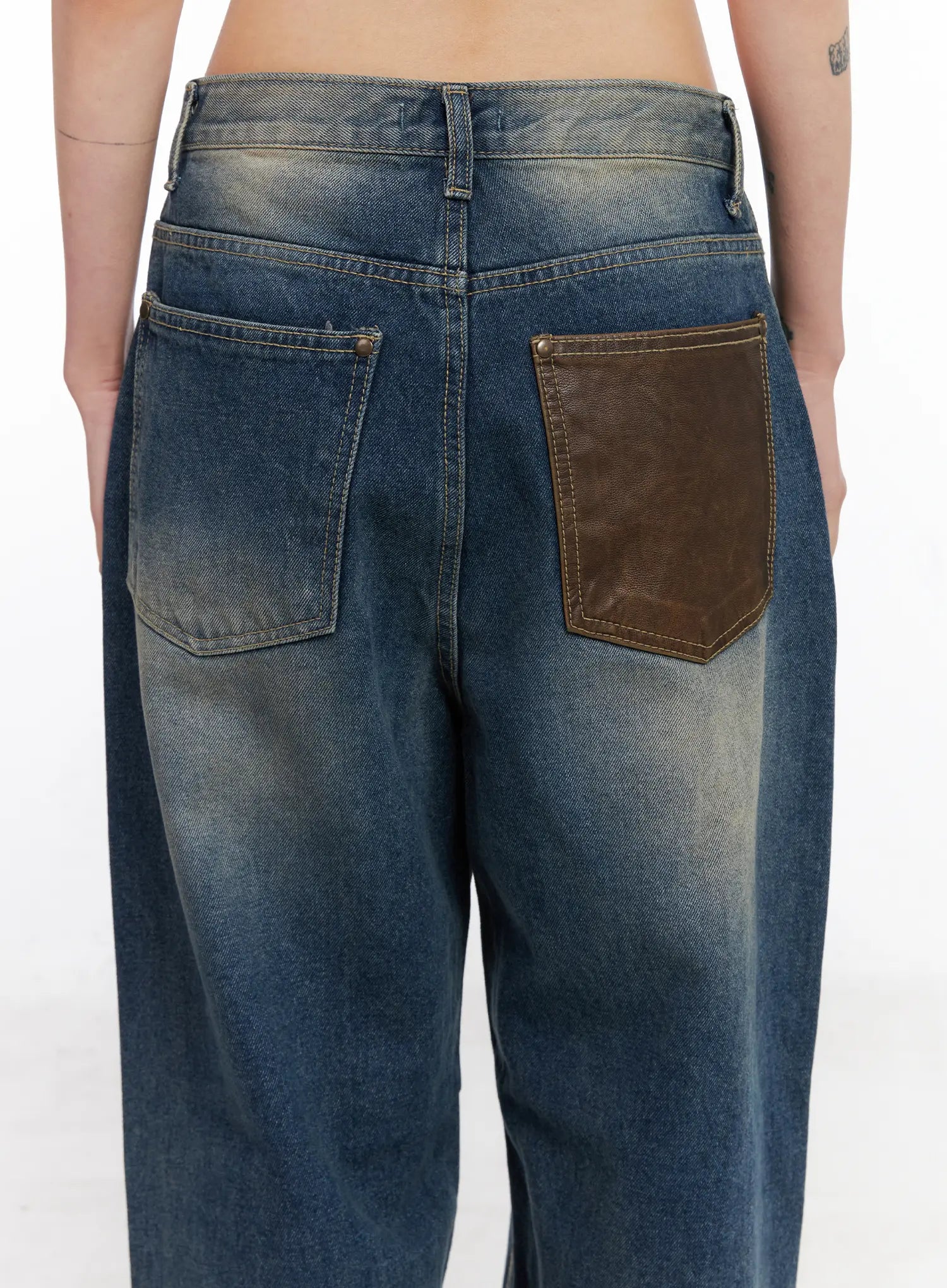 Xyla Vintage Pocket Baggy Jeans CO507 in blue, close-up back detail on model, featuring contrast brown leather patch pocket with gold rivets and washed denim texture.