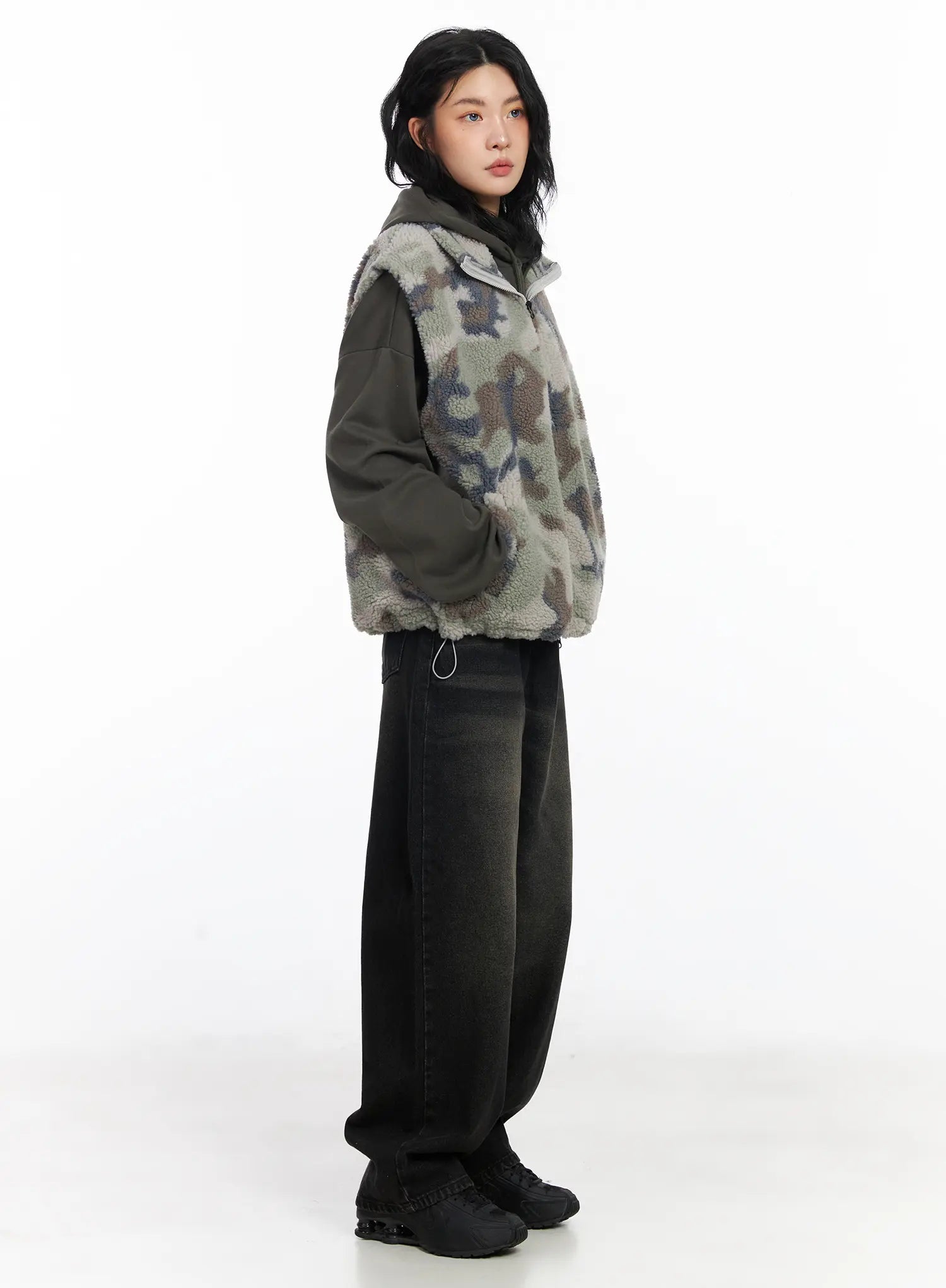 Dayana Vintage Washed Wide-Leg Jeans CJ523 in black, side full-body editorial shot, model in profile, layered with camo fleece vest and hoodie, wide-leg hem breaking over sneakers.