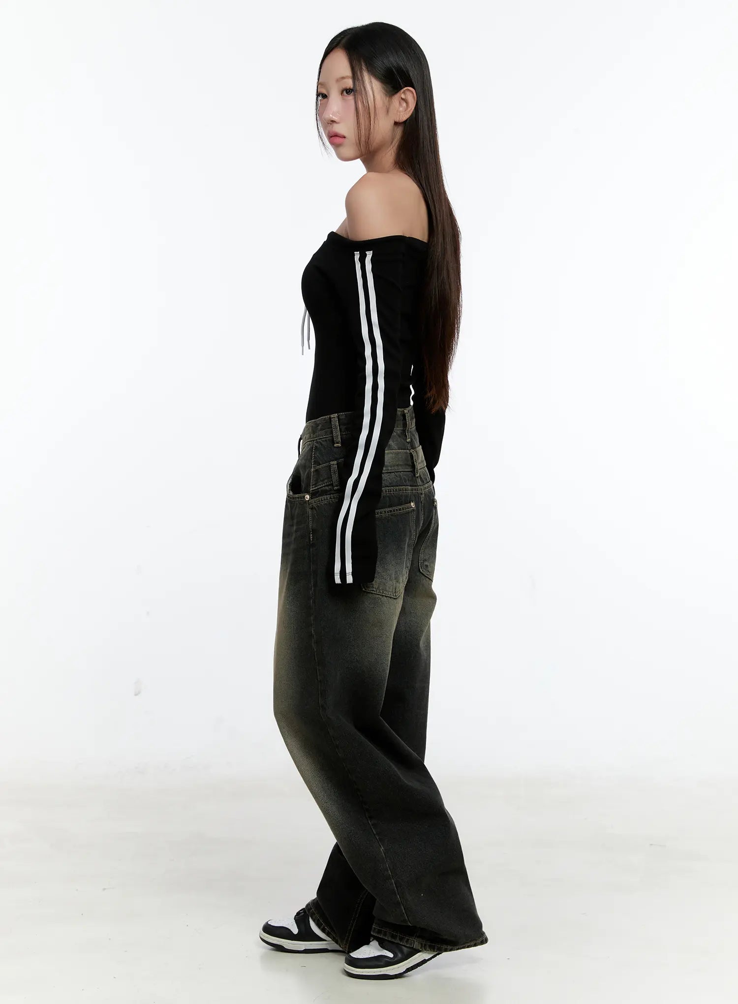 Emerie Washed Wide-Leg Baggy Jeans CS518 in dark blue, three-quarter side view on model, highlighting wide-leg drape and waist pocket placement, styled with black stripe off-shoulder top and sneakers.