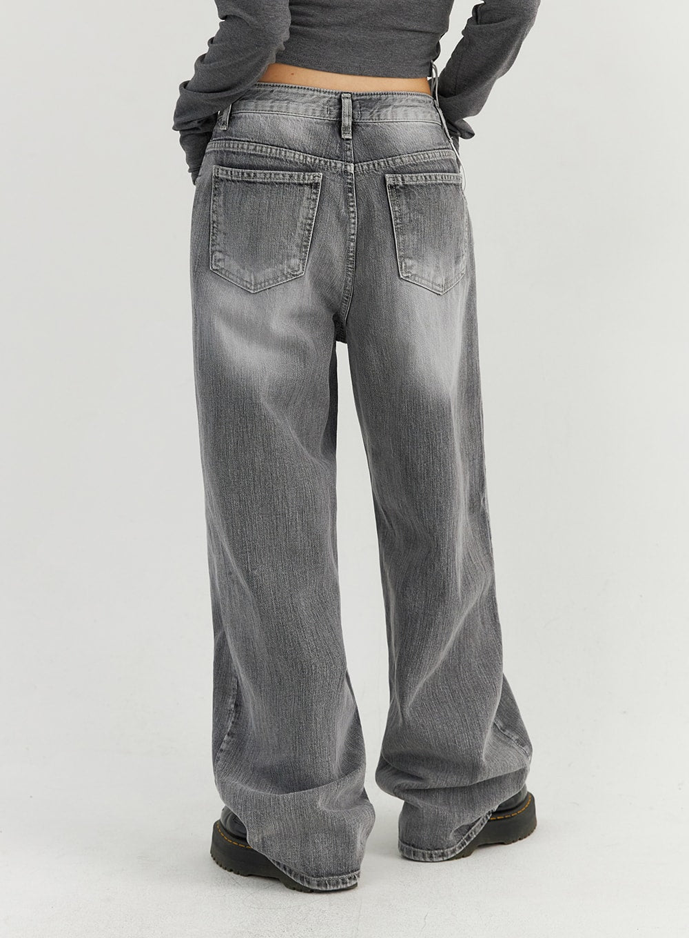 Grey Washed Wide Leg Jeans CO323 in Gray, back waist-down close-up on model, highlighting dual back patch pockets with faded wash and wide-leg floor-length hem pooling over boots.