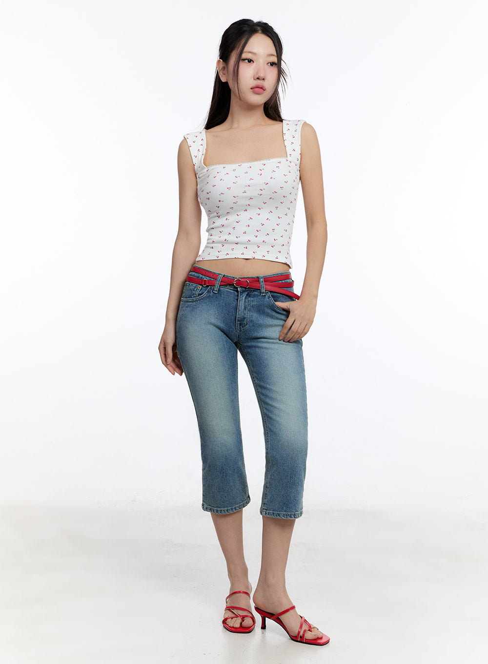 Kyra Cropped Low-Rise Skinny Jeans IU503 in blue, full-body front on model with red belt styled loosely at waist, washed denim skinny crop, paired with white floral tank and red heeled sandals.