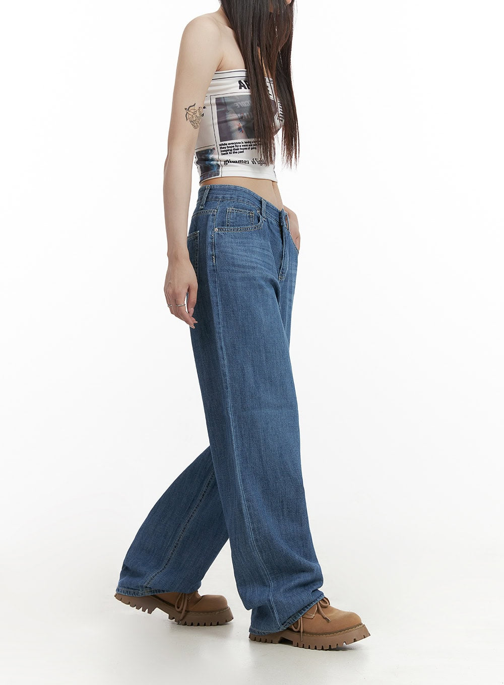 Solid Low Rise Baggy Jeans CY407 in blue, walking side-angle shot on model, wide-leg washed denim with low waist and slight pooling at hem, styled with graphic bandeau and tan boots.