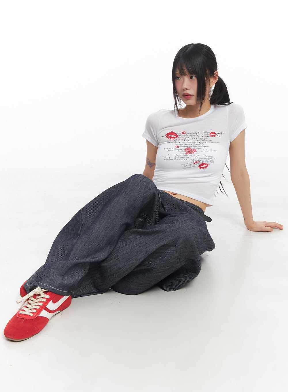 Isabel No-Fade Baggy Jeans CY514 in dark blue, seated floor pose on model, voluminous baggy cotton denim pooling around legs, paired with white graphic crop tee and red sneakers.