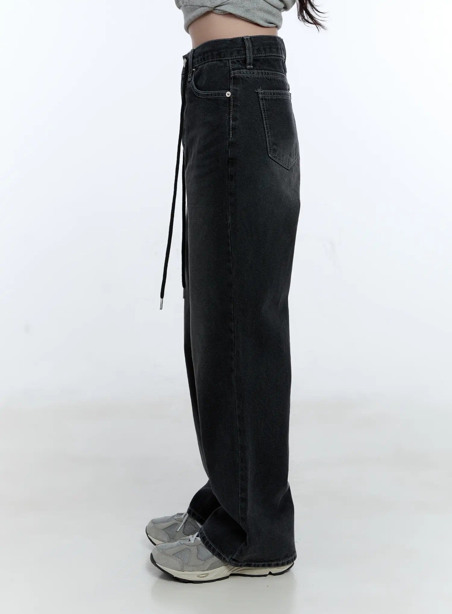 Lucinda High-Rise Wide Leg Jeans CG512 in black, side view on model, washed denim highlighting wide leg drape and dangling drawstring cord, side pocket visible, paired with gray crop top and sneakers.