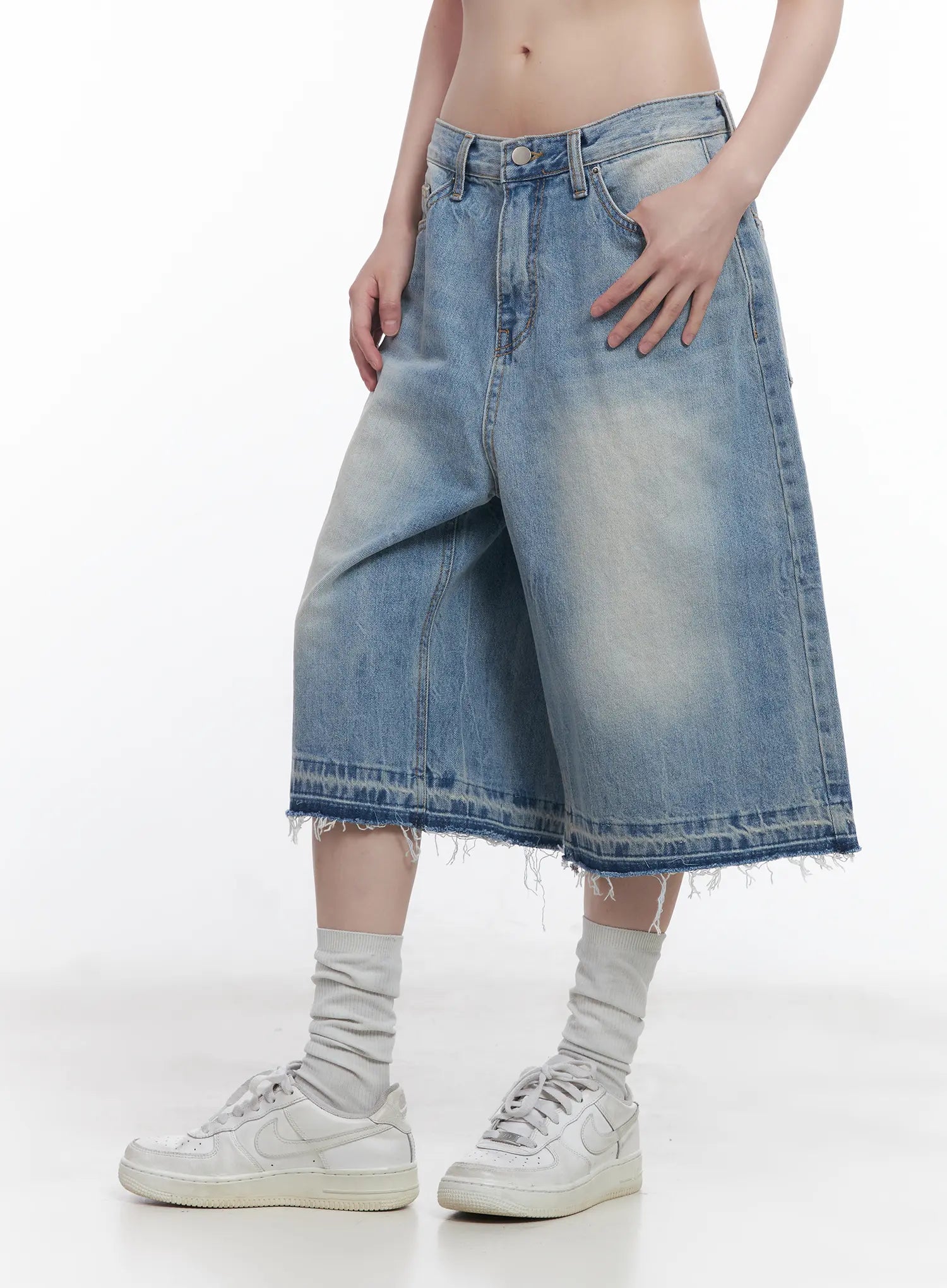 Light Wash Vintage Jorts CU519 in blue, side close-up on model from waist down, low-waist wide-fit denim with heavy vintage wash fading and raw frayed cutoff hem, white sneakers.