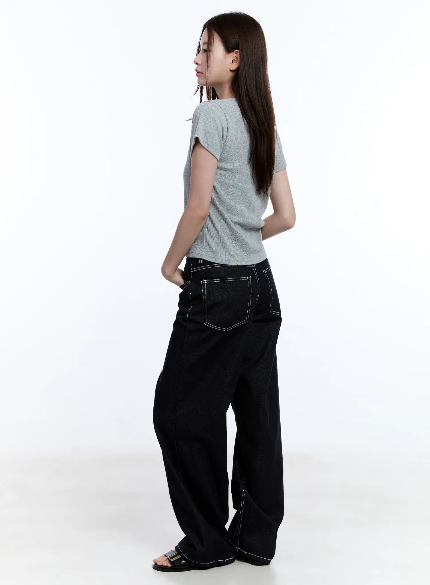Nayeon No-Fade Denim Jeans CU513 in dark blue, side-angle view on model, showing wide-leg silhouette and contrast-stitched back pocket, paired with grey tee and buckle sandals.