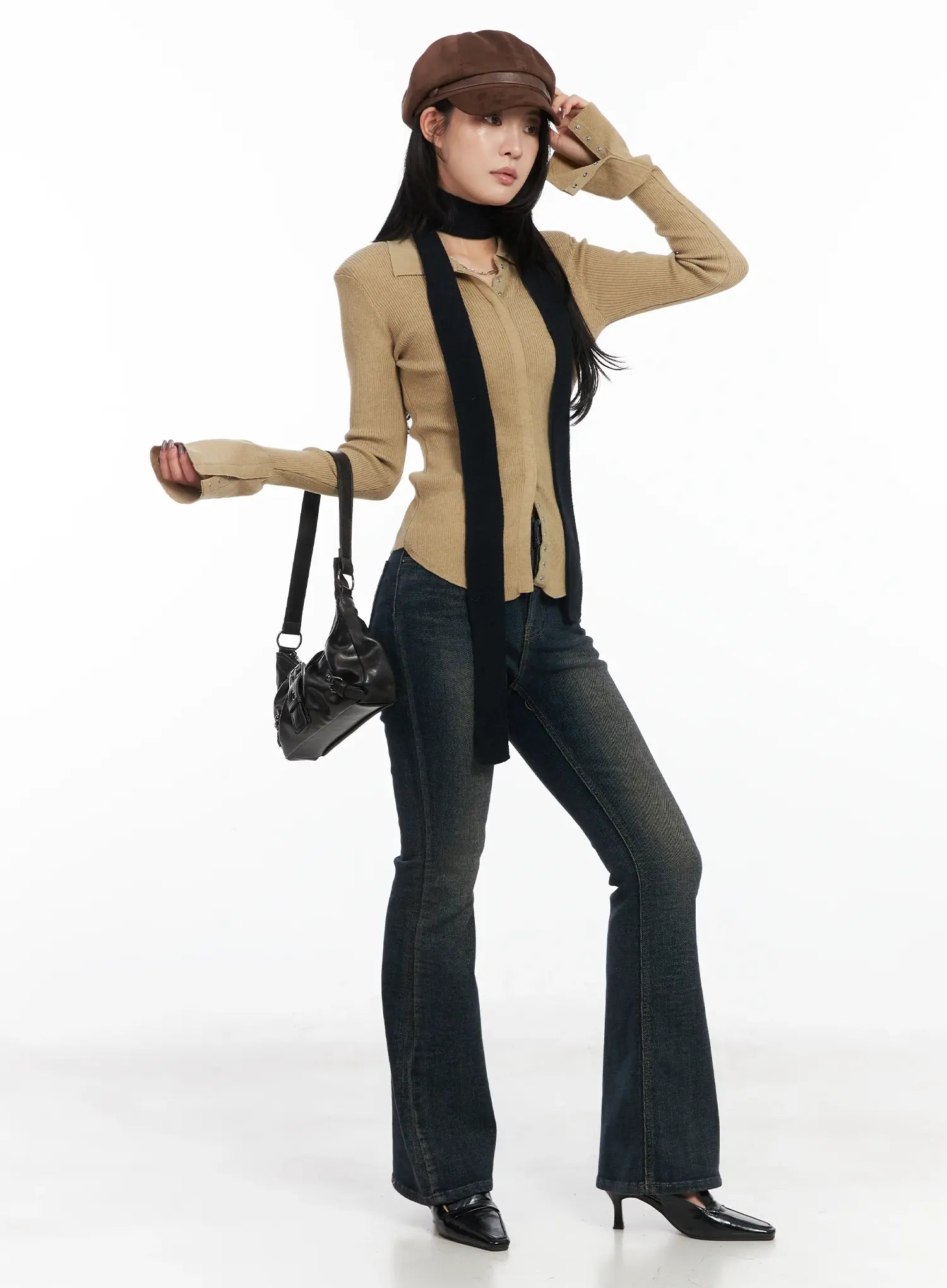 Jordyn High-Waist Bootcut Jeans CD502 in dark washed indigo, three-quarter front view on model in dynamic pose, full-length bootcut leg, styled with camel knit top, black scarf, and brown leather cap.