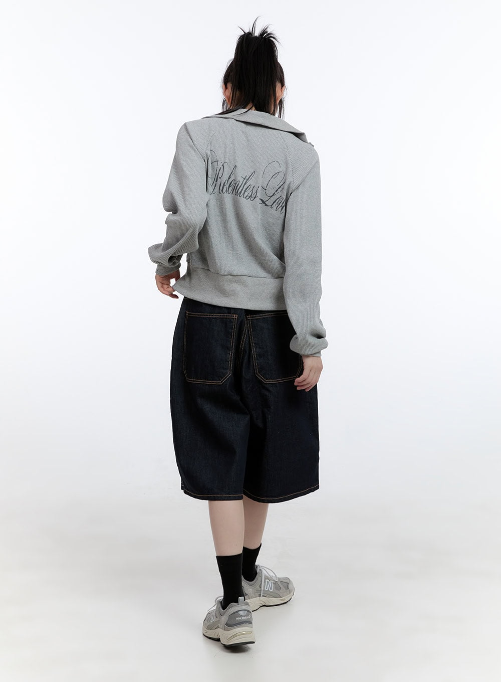 Dora Stitched Baggy Jorts CG413 in dark blue, back full-body shot on model, showing large patch back pockets with contrast stitching, styled with grey graphic zip top and sneakers.