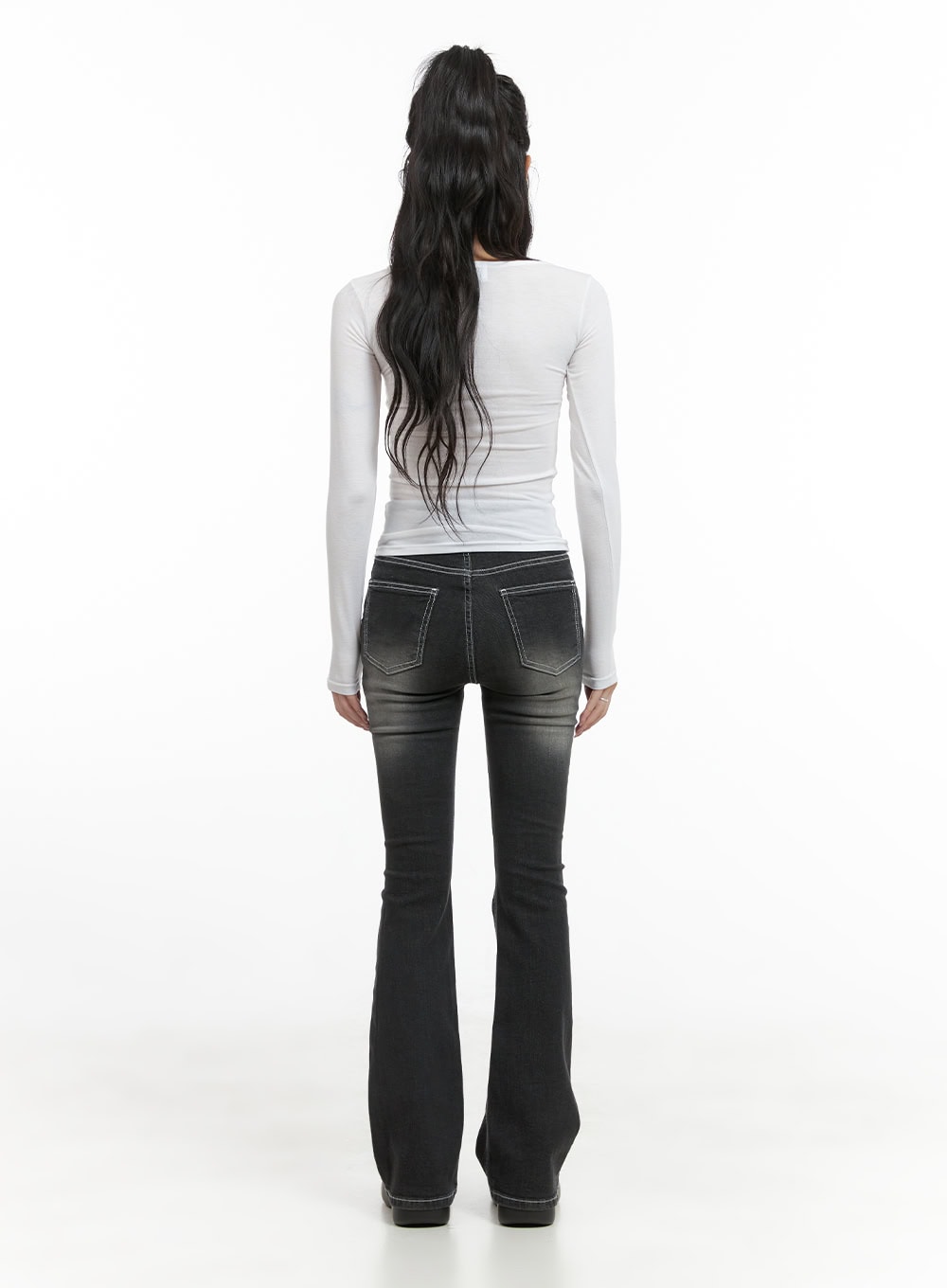 Gigi Two-Button Slim Bootcut Jeans CG421 in black, back full-length shot on model with high ponytail, showing bootcut flare silhouette, contrast-stitched back pockets, and washed denim fade, paired with white long-sleeve top.