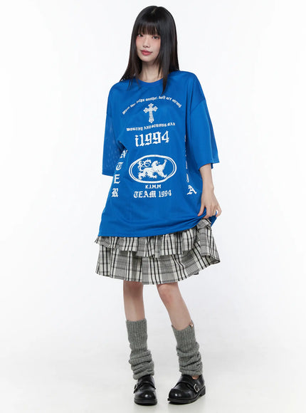 Plaid Layered Midi Skirt CU519 in black, full-length front shot on model standing, layered ruffle hem peeking below oversized blue graphic tee, grey leg warmers and Mary Jane shoes.