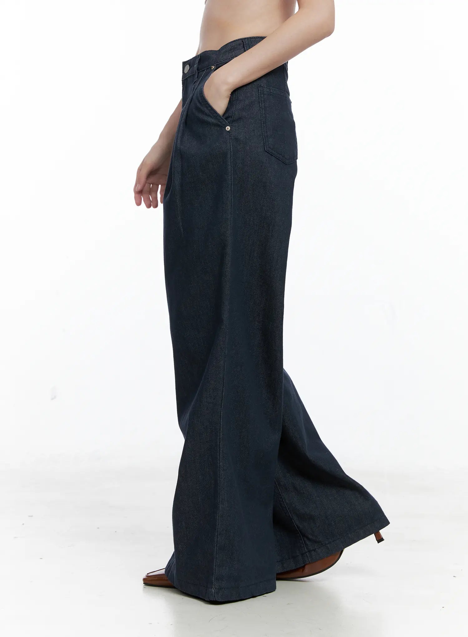 Lena Pintuck Baggy Jeans CO503 in dark blue, side view on model, showcasing high waist, side pocket, and dramatic wide flared hem in cotton denim, worn with brown mule heels.