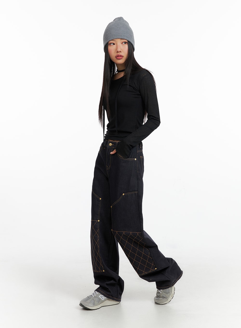 Stitched Wide Denim Jeans CF408 in dark navy, three-quarter front view on model with relaxed walking pose, wide-fit floor-length denim with gold studs and amber diamond stitch, styled with black crop top and beanie.
