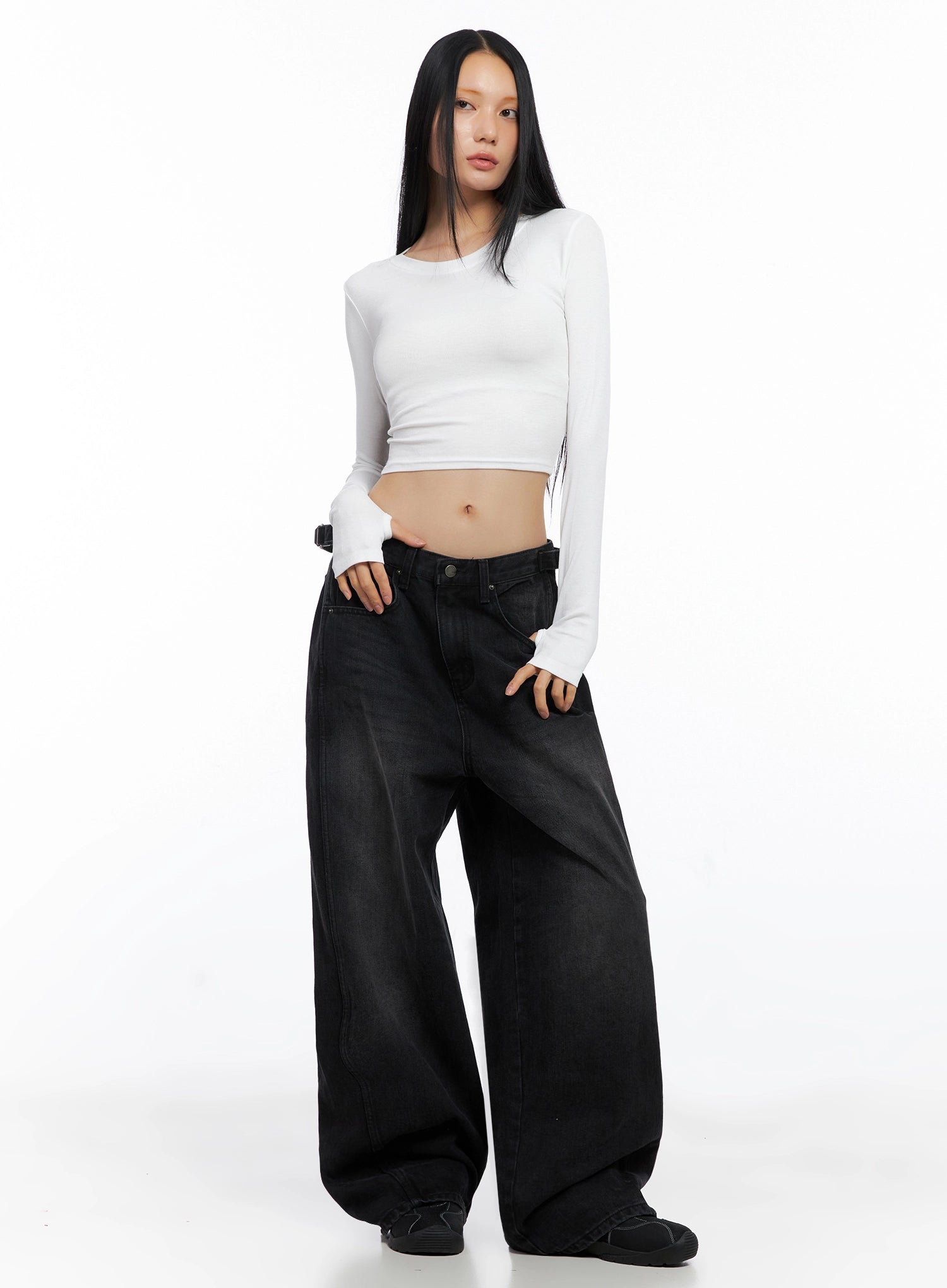 Goffel Side Belt Washed Wide Denim Pants IO517 in black, full-body slightly angled front shot on model, low-rise wide leg with side belt, paired with white crop top and black sneakers.