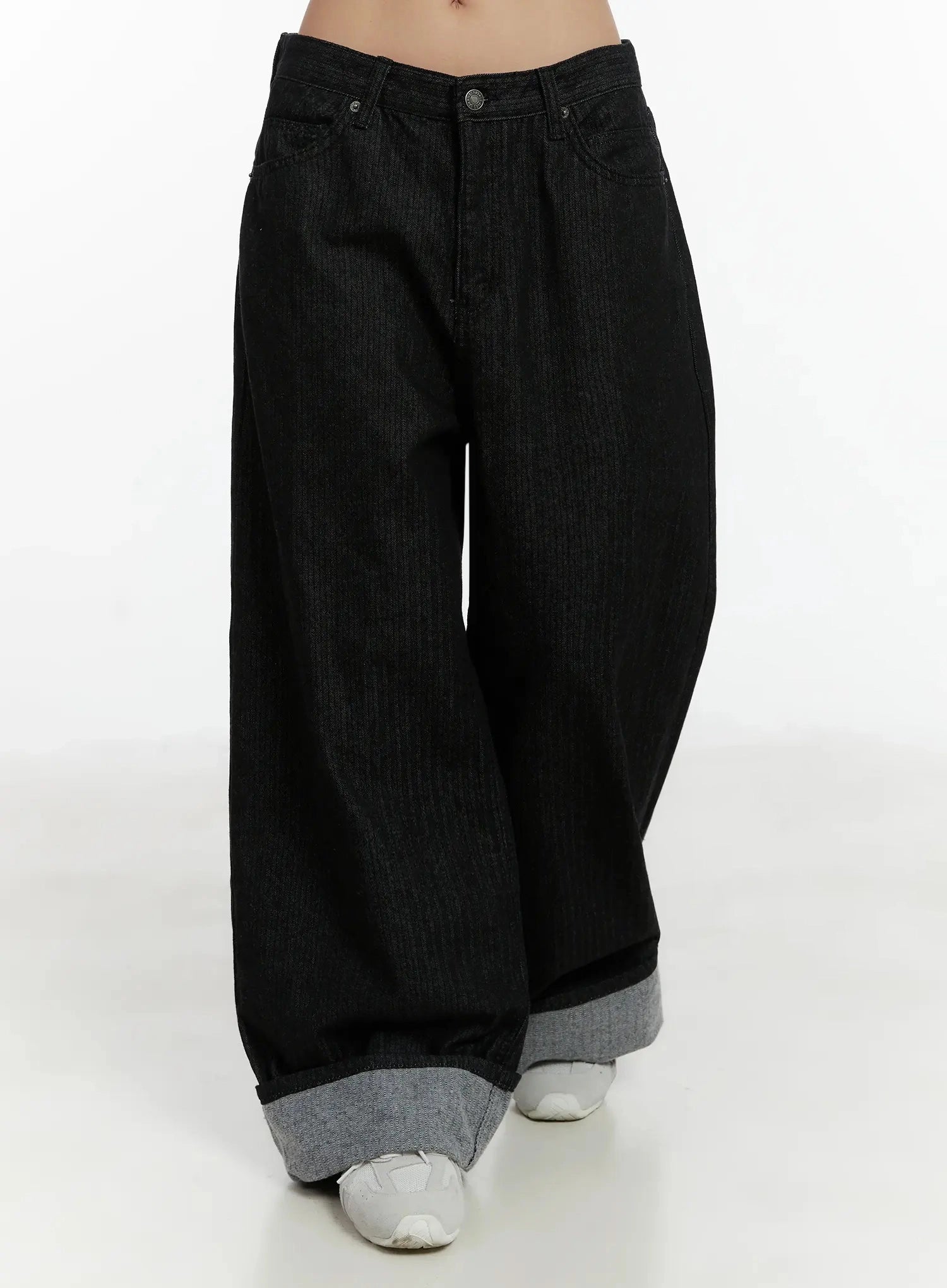 Amyra Baggy Striped Jeans ID525 in black, front mid-shot on model, baggy wide-leg silhouette with contrast grey rolled cuff hem, vertical stripe texture, white sneakers visible.