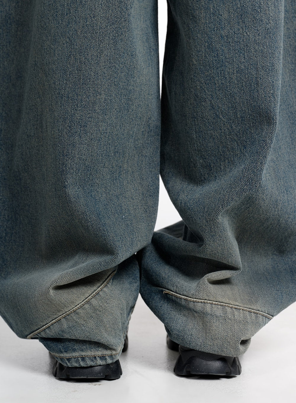 Vintage Low Rise Baggy Jeans CM415 in dark blue, close-up of hem and leg opening, showing extreme wide-fit pooling at ankle, washed denim with contrast stitching, worn with chunky black sneakers.