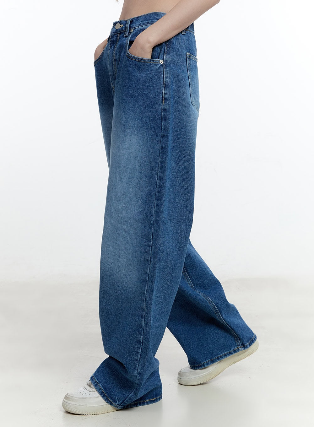 Eugene Adjustable Cinched-Back Wide-Leg Jeans CM521 in dark blue, side close-up on model mid-stride, washed cotton denim with wide-leg drape and front pocket detail, white sneakers visible at hem.