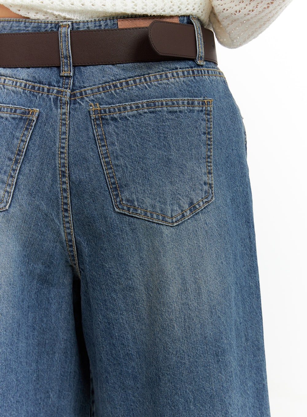 Vintage Washed Wide Leg Jorts CA415 in blue, back pocket close-up, vintage-washed cotton denim with gold topstitching on patch pocket and faded wash texture, brown leather belt.