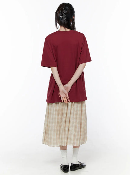 Oversized Graphic Print Tee CU519 in dark red, full-length back view on model, plain clean back with drop shoulders and slightly elongated hem, paired with beige plaid midi skirt and black Mary Jane shoes.